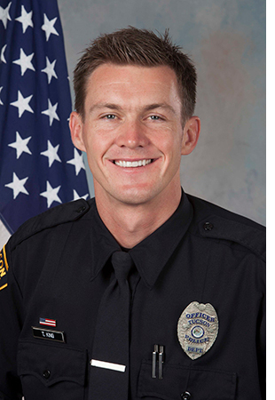 Department photo of TPD officer in uniform, smiling in front of an American flag.