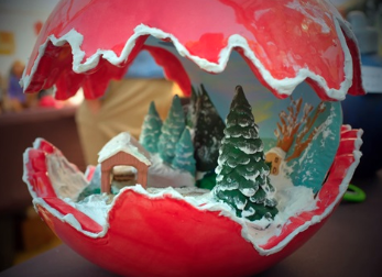 Picture of house and some pine trees covered with snow inside of the red Christmas ornament