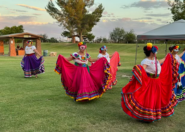 Women dancing folklorico outside on grass at park.