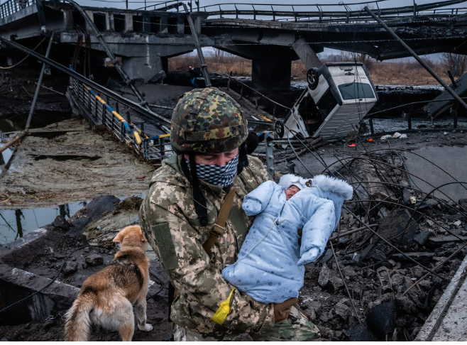Picture shows a Ukraine soldier carry a baby with destroyed bridge and van as a background 