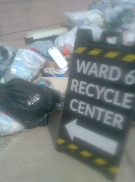 Picture shows recycle center signage at ward 6 with some plastic bags next to it 