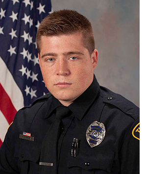 Department photo of TPD male officer in uniform in front of American flag.
