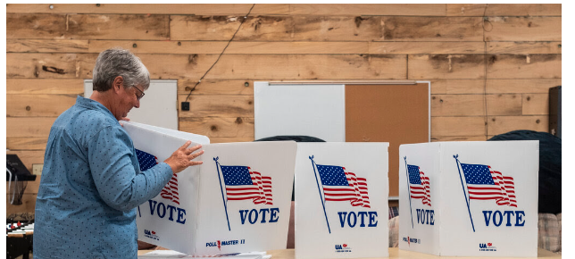 A lady in the blue long sleeve shirt prepares voting booth for in person voters 
