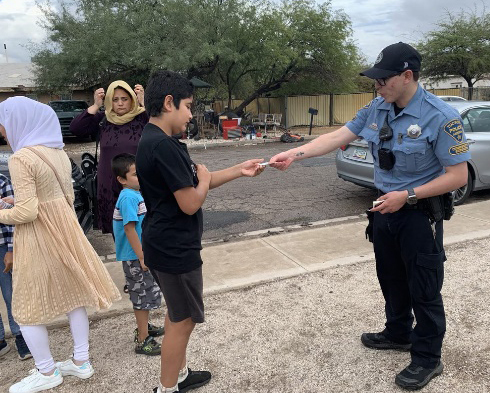 A uniformed TPD CSO hands information to a youth outside, other family members in the background.