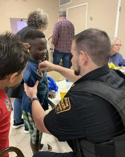 A uniformed TPD officer, back to the camera, puts a badge sticker on a little boy.