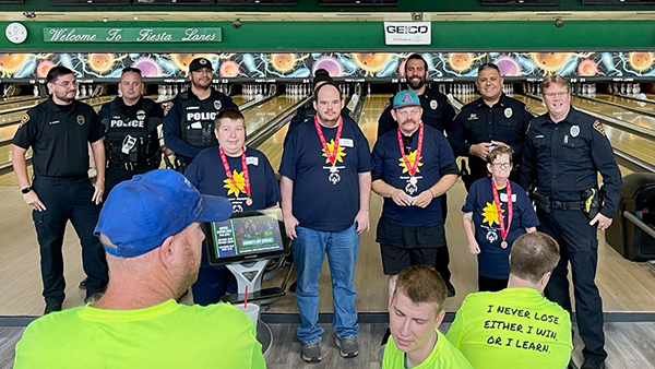 Uniformed TPD officers and Special Olympics athletes pose for a group photo in front of bowling lanes.