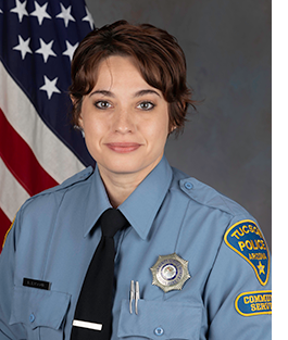 A uniformed female Community Service Officer sits for a Department photo in front of an American flag.