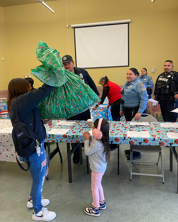 A young woman and a little girl receive a giant bag of Christmas cheer. Uniformed TPD members stand in the background.