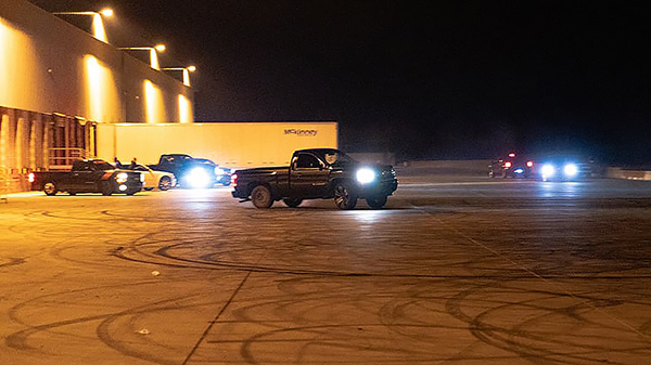 Nighttime at a commercial parking lot, trucks doing stunts and leaving tire tracks on the asphalt.