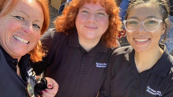 Three smiling women, in Tucson Police Department polo shirts, take a selfie outdoors in the sunshine.