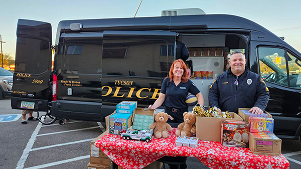 TPD members in uniform stand behind a table with toys and teddy bears in front of a TPD van