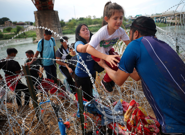 A man helps a mother to carry her daughter to cross the barbered wire fences 