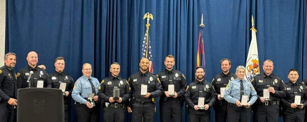 Long line of TPD members holding their awards in front of a blue curtain, Chief Kasmar at the far left. 