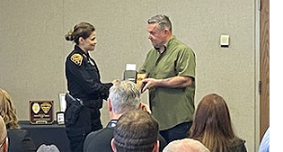Female deputy chief in uniform hands retirement credentials to a male in civilian clothes.