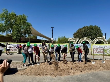 Image of groundbreaking with 10 officials in green hard hats using shovels to move loose dirt.