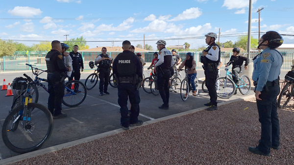 TPD members in uniform stand in the shade around bicycles in a school parking lot.