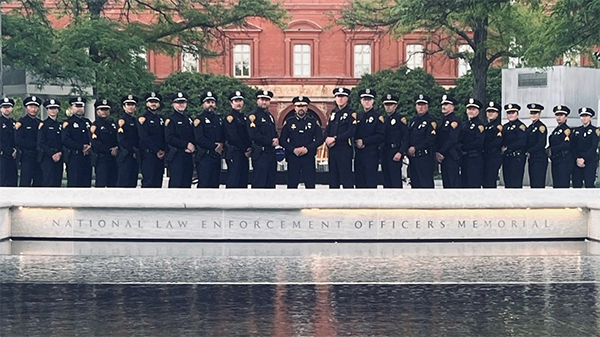 Line of TPD sworn members in dress uniform standing behind a reflecting pool and a low engraved stone wall.