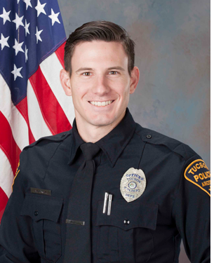 Department photo of smiling TPD officer in uniform in front of an American flag.