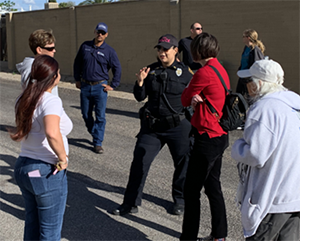 A uniformed TPD officer stands in a parking lot speaking with community members.