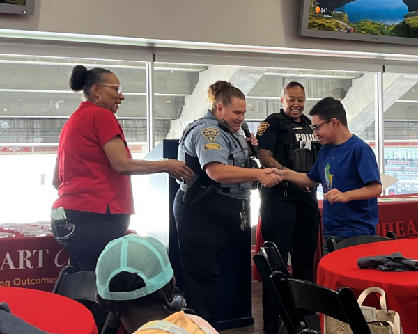 TPD CSO and officer congratulate a young student in a school cafeteria.