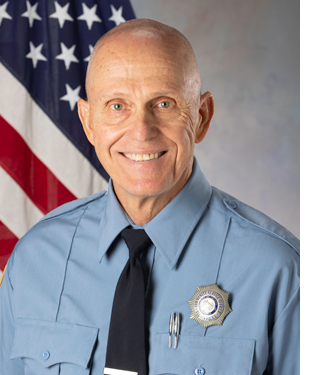 Department photo of CSO in uniform in front of an American flag.