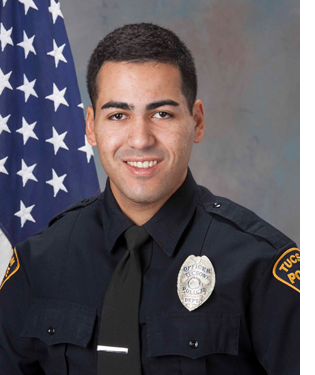 Department photo of officer in uniform in front of an American flag.