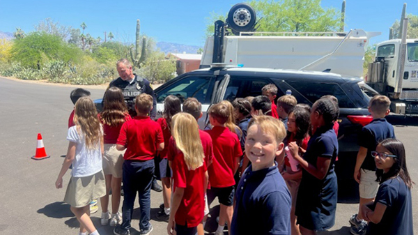 Children outside on a street with a TPD officer in uniform and mountains in the background.
