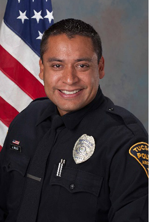 Department photo of uniformed officer in front of an American flag.