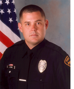 Department photo of a TPD officer in uniform in front of an American flag.