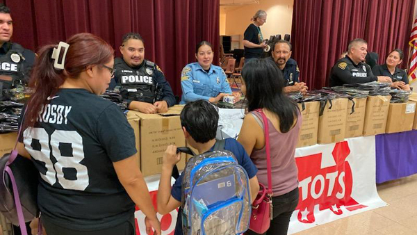 A parent and children stand in front of a Toys for Tots table staffed by TPD members in uniform.