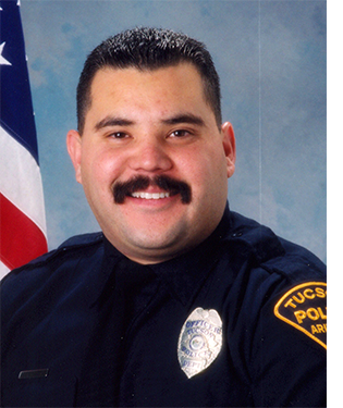 Department photo of TPD officer in uniform in front of an American flag.