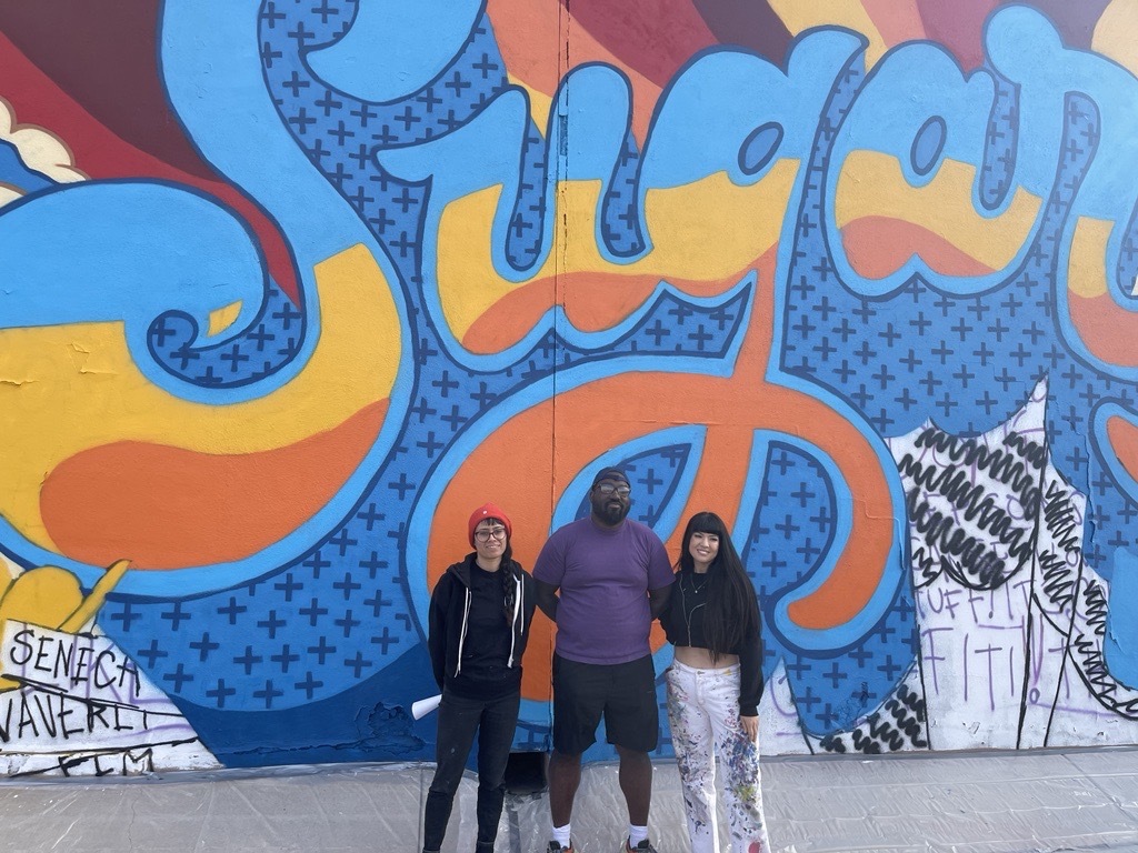 Photo of Mural artist Ndubisi Okoye (middle) with his team Allison (left) and Jessica (right).