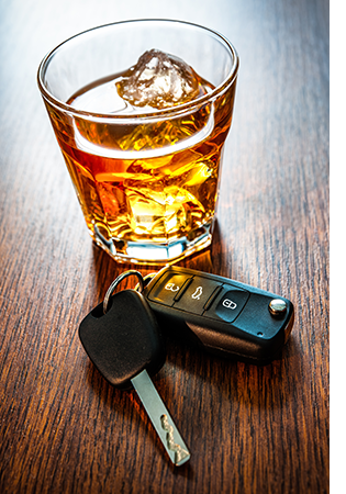 Brown liquor on the rocks and car keys on a wooden tabletop.