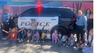 Young children sit on the ground in front of a TPD patrol vehicle, their teacher and TPD personnel stand with them.