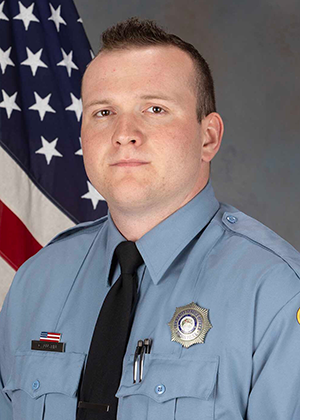 Department photo of a CSO in uniform in front of an American flag.