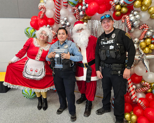ODS members in uniform pose with Santa and Mrs. Claus in front of a holiday display of balloons and giant candy canes.