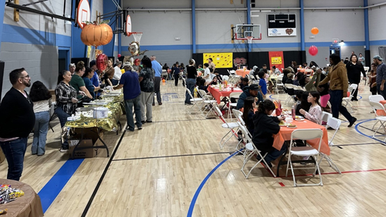 People sit in small groups at tables set up in a gymnasium.