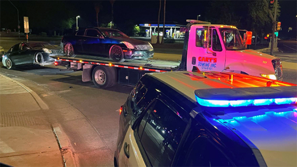 Nighttime: two cars are towed away while a patrol vehicle with lights on is in the foreground.