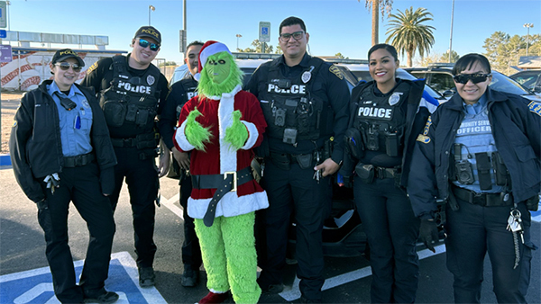 The Grinch, in Santa attire, stands outside with TPD officers and CSOs in uniform.