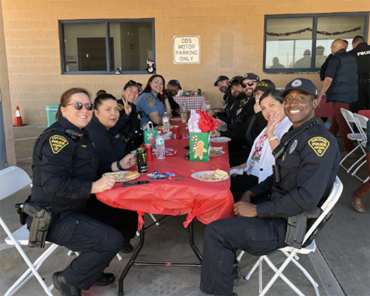 Smiling TPD officers in uniform sit at a table, outdoors, enjoying a holiday meal.