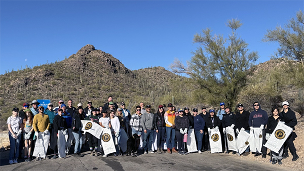 People stand with trash bags for a group photo in the desert, hills in the background.
