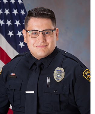 Department photo of a TPD officer in uniform in front of an American flag.