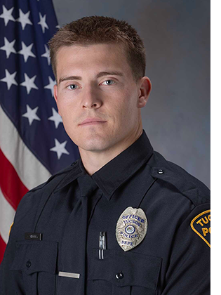Department photo of officer in uniform in front of an American flag.