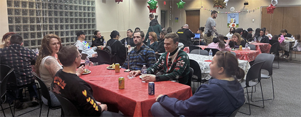TPD members and families sit at folding tables in a large room with holiday decorations.
