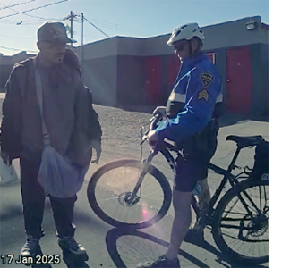 TPD bike officer in uniform contacts a man standing in the street.