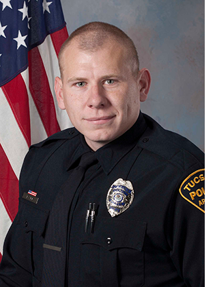 Department photo of TPD officer in uniform in front of an American flag.