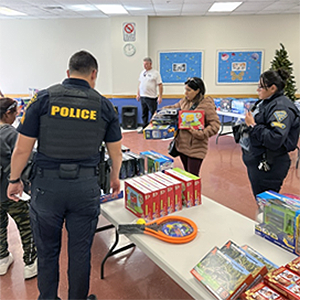 Uniformed TPD officer and CSO stand by a table with toys as a parent looks on.