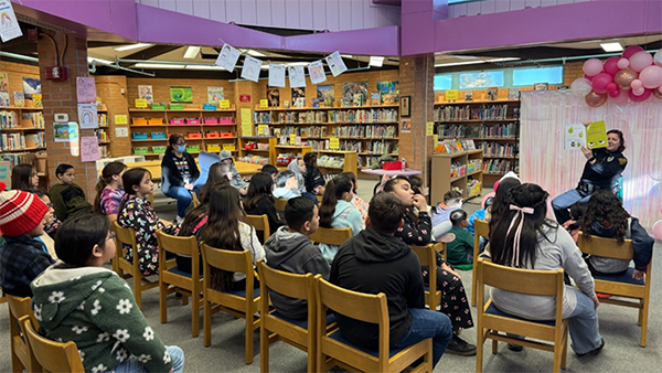 A uniformed TPD female officer holds up the book as she reads to children in a school library.