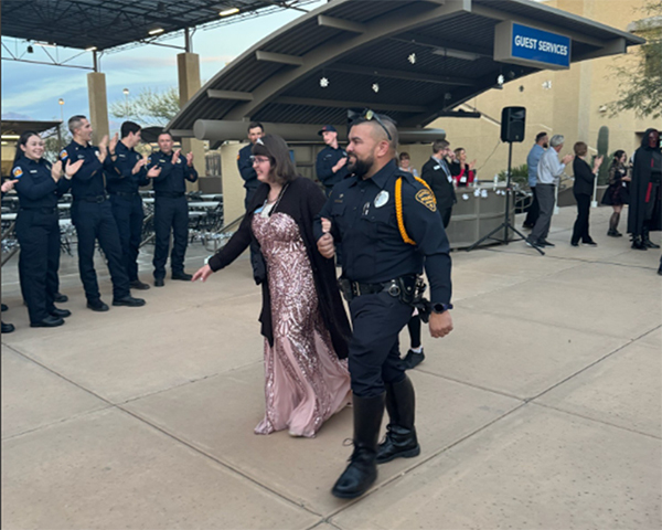 A uniformed male officer escorts a woman in an evening gown to an event as other officers applaud.