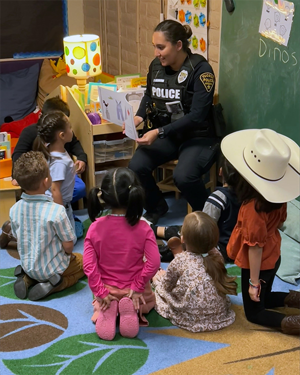TPD female officer in uniform reads to young children, who sit on a brightly colored carpet in front of her.